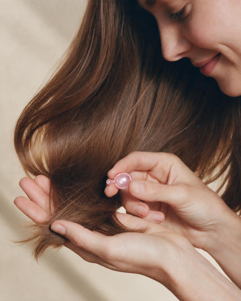 Kädet pitelevät pehmeitä, kiiltäviä hiuksia ja yhtä Ellips Hair Repair -kapselia