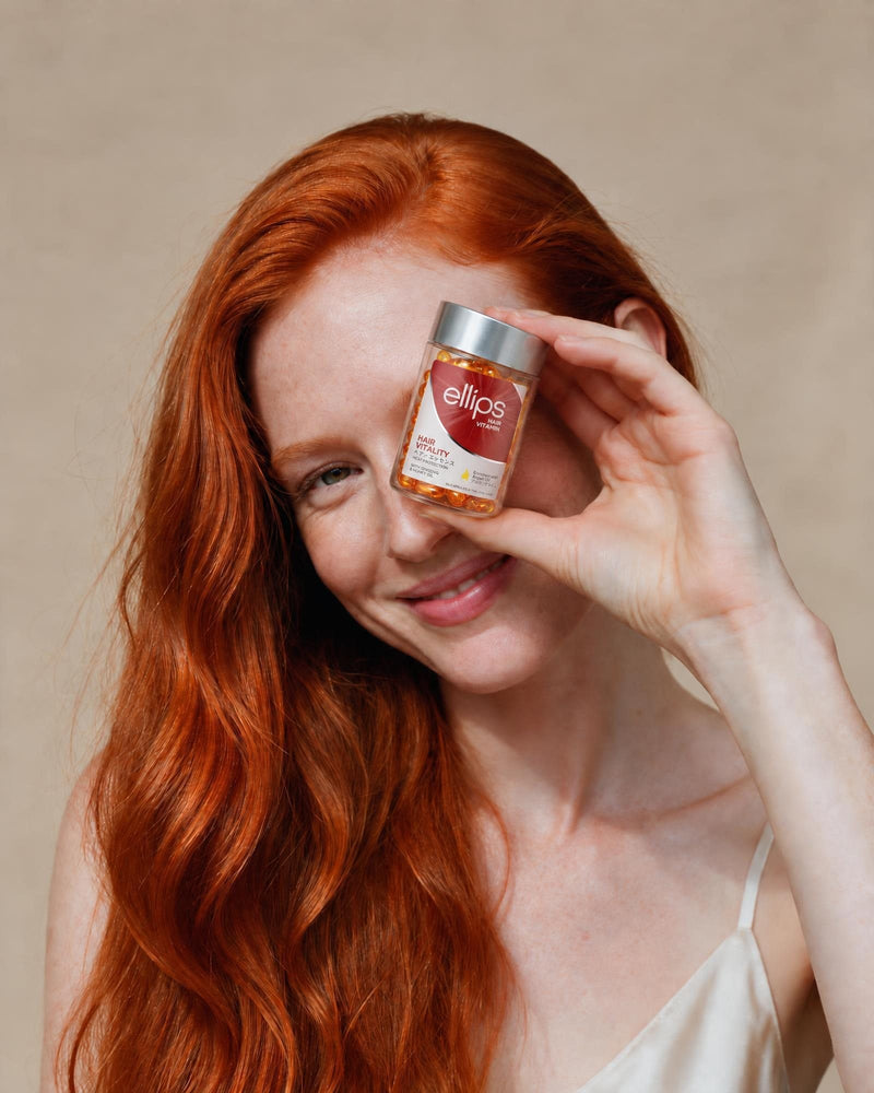 Nainen, jolla on pitkät kuparinväriset hiukset, pitelee Ellips Hair Vitality -purkkia