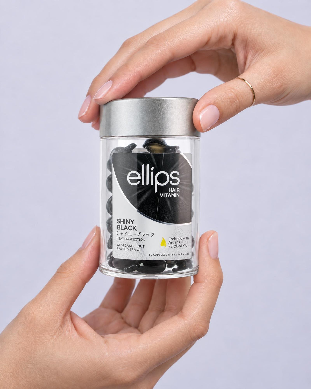 Kaksi kättä pitelee Ellips Shiny Black -purkkia