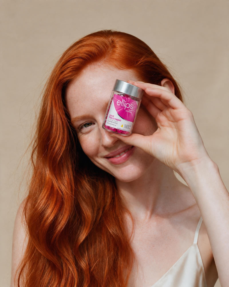Nainen, jolla on pitkät kuparinväriset hiukset, pitelee Ellips Hair Treatment -purkkia